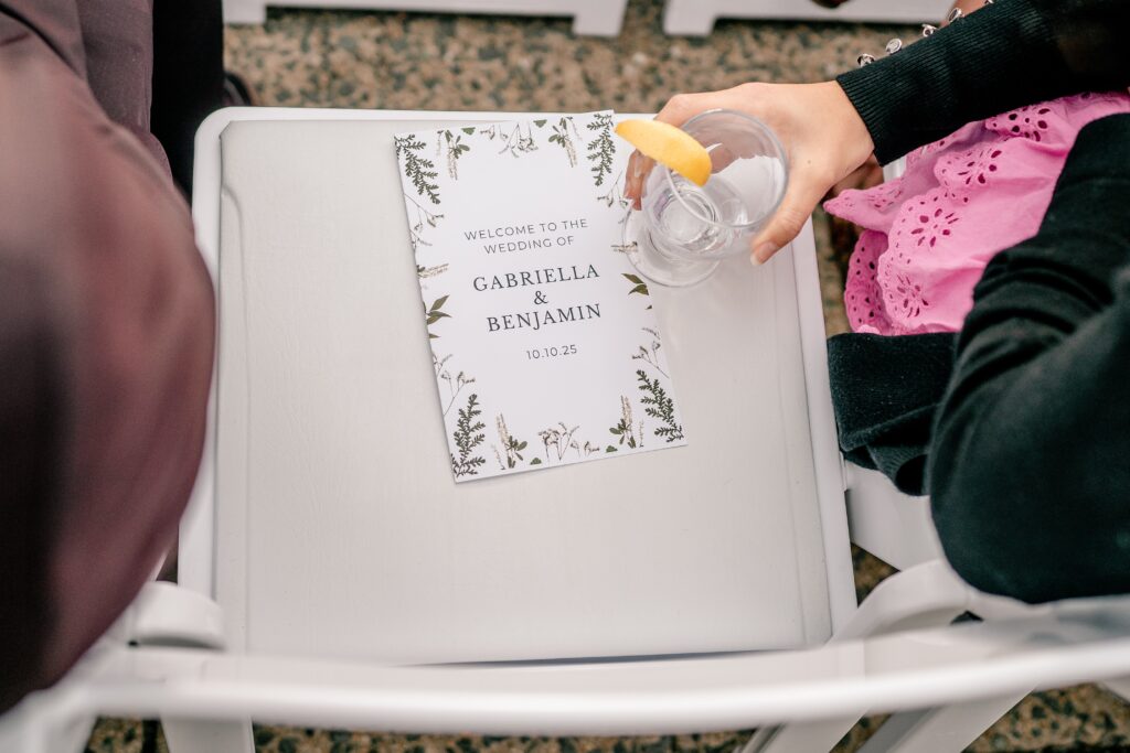 A guest placing a drink on an empty seat with a wedding program on it before a Meadowlark Botanical Gardens wedding