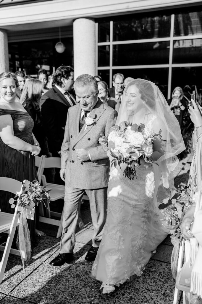 A bride and her dad walk down the aisle to start her Atrium at Meadowlark wedding