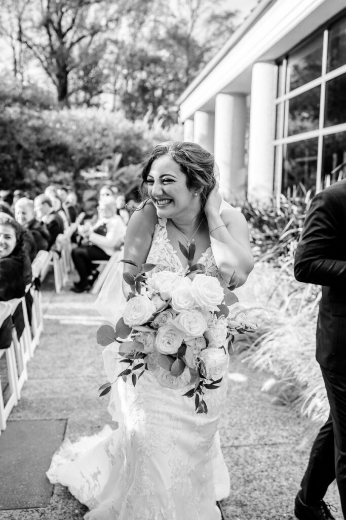 A bride smiles authentically at her guests as she leaves her ceremony captured by a Northern VA wedding photographer