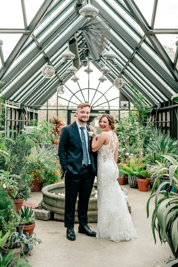 A bride and groom pose happily inside their greenhouse wedding venue in Virginia