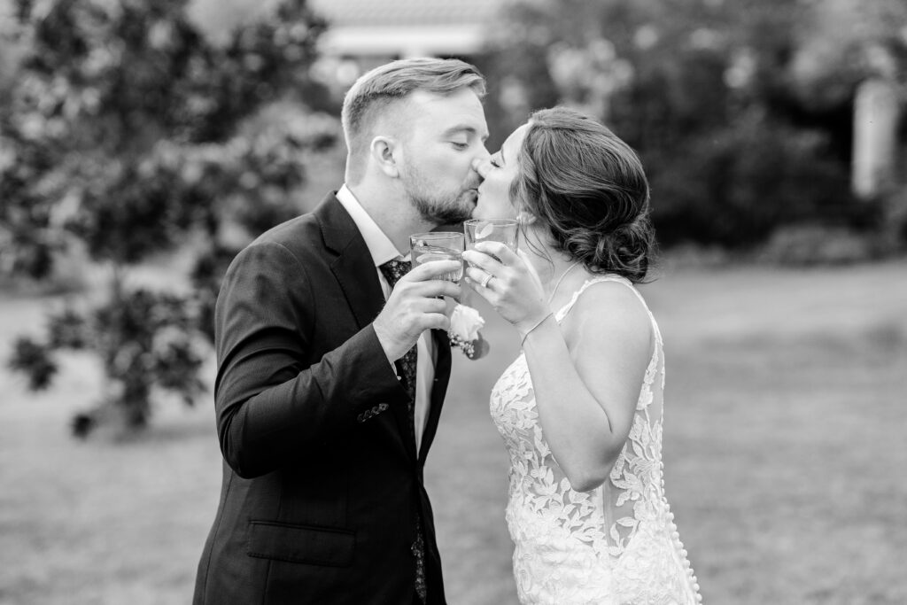 A bride and groom share a kiss with their cocktails during an Atrium at Meadowlark wedding