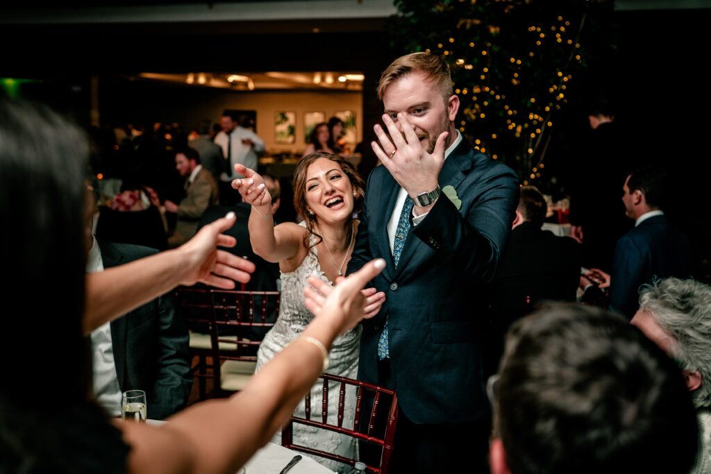 A bride and groom show off the groom's new ring to guests