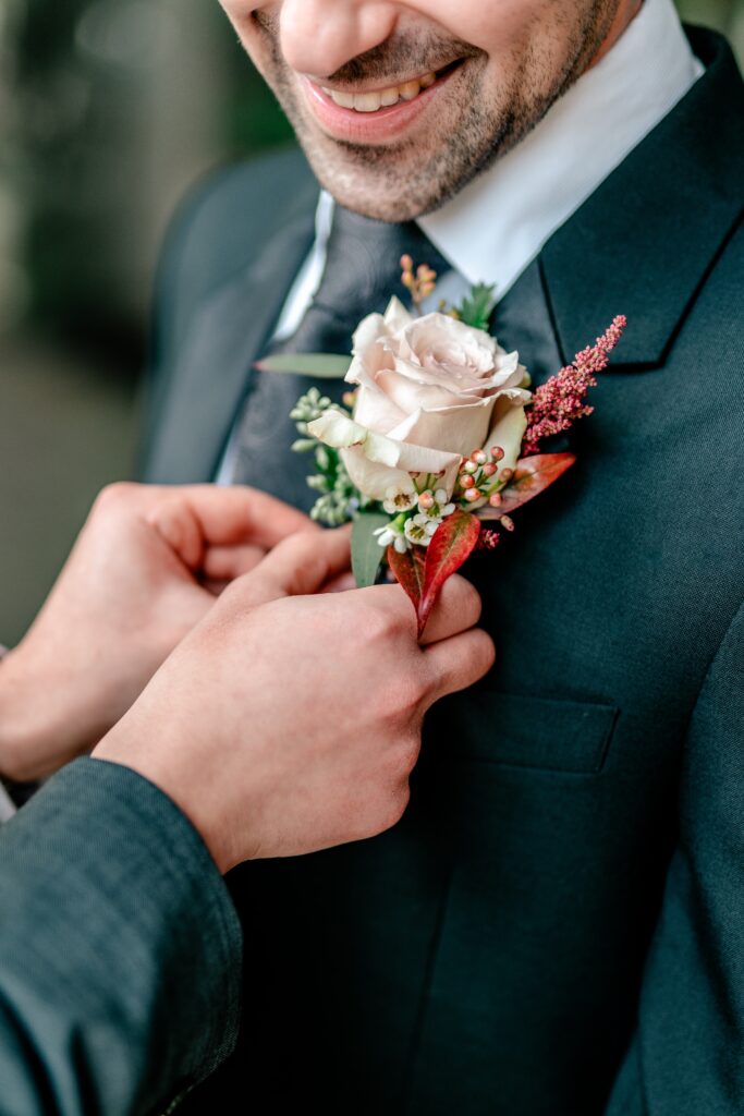 A close up of a boutonnière being pinned on a groom taken by a Northern VA wedding photographer