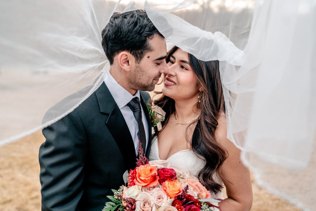 A bride and groom smiling at one another under her veil