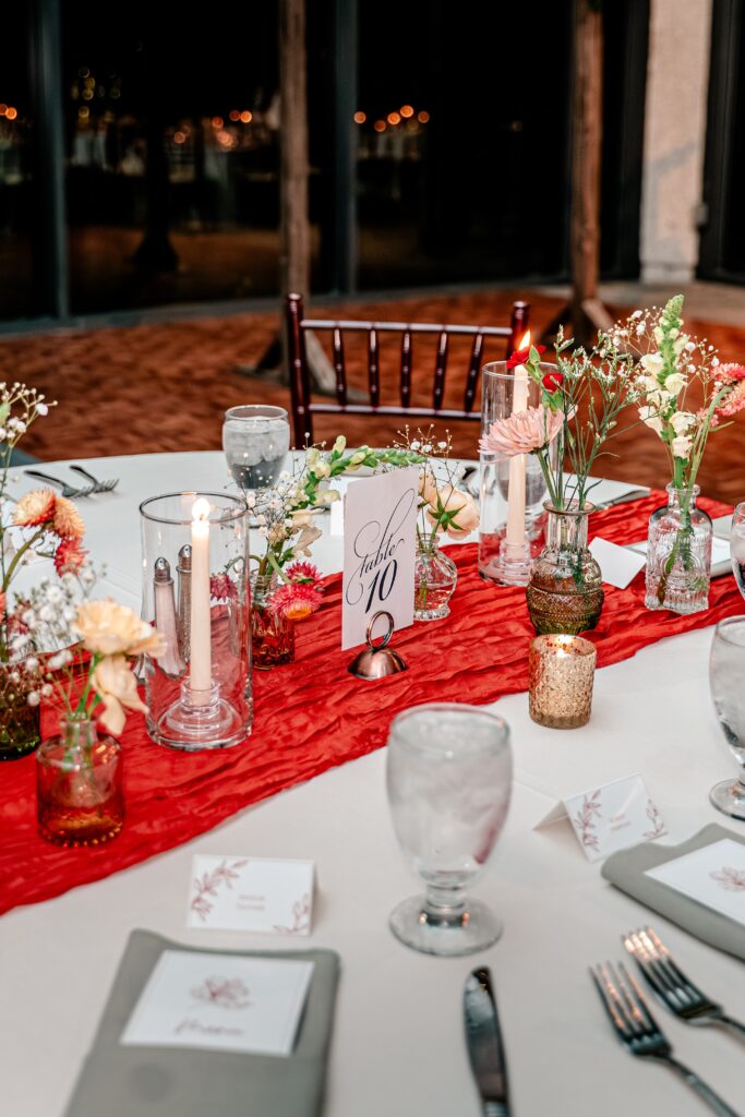 A November wedding reception table set with flowers and a red table runner
