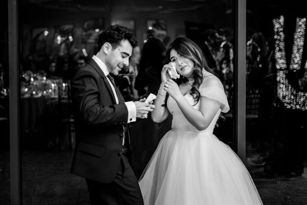 A bride and groom wipe tears during their Atrium at Meadowlark indoor wedding reception