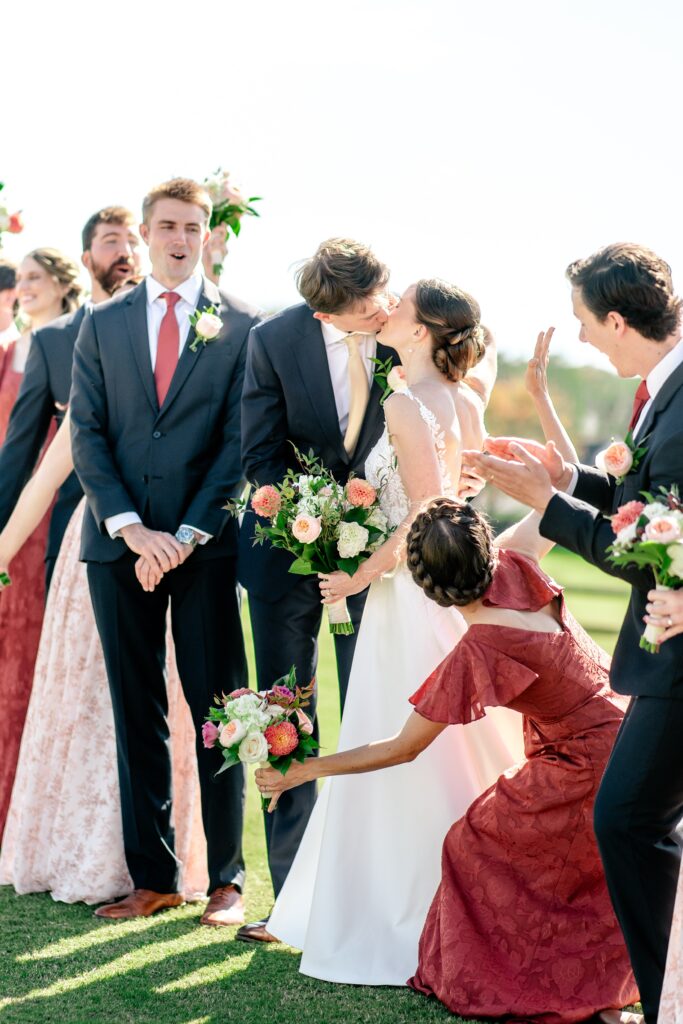 A wedding party cheers on a bride and groom sharing a kiss