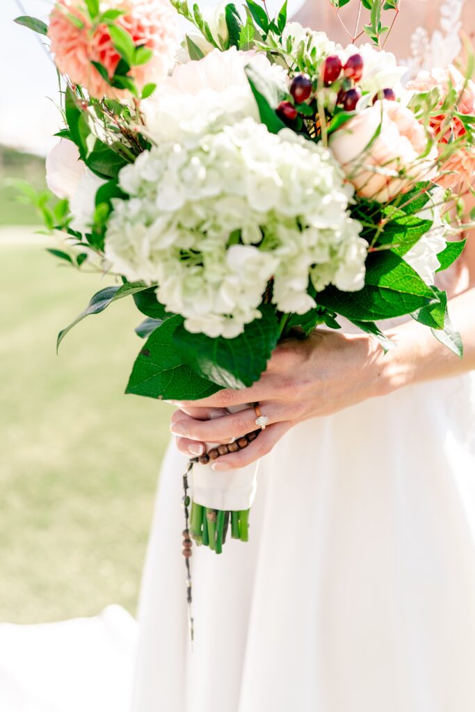A bridal bouquet with focus on the bride's engagement ring and rosary hanging down the stems during a The Estate at Independence wedding
