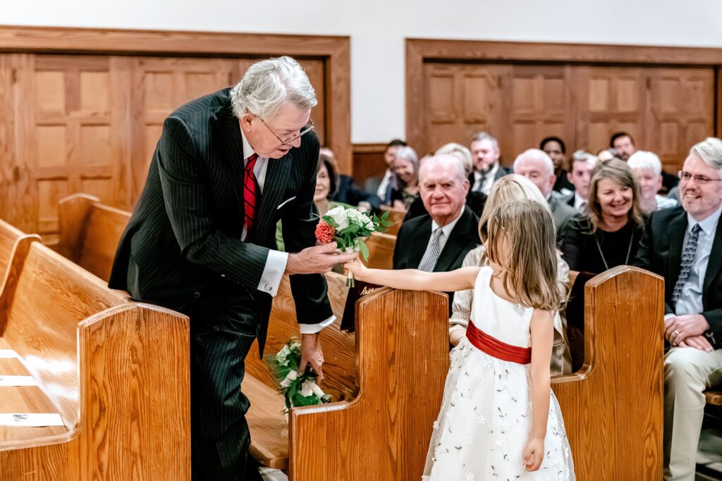 A flower girl hands off flowers for the groom's dad in front of the Richmond wedding photographer