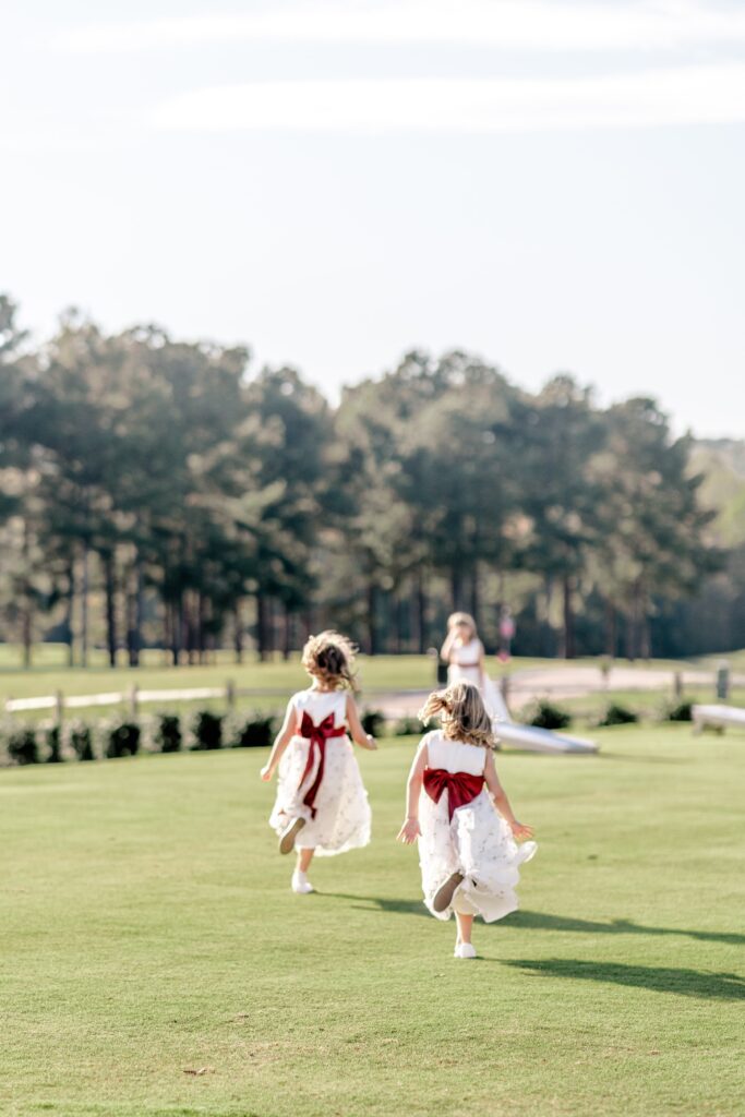 Flower girls running across an open field away from their Catholic wedding photographer