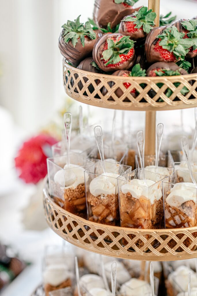 A tiered tray of desserts including pie shooters and chocolate covered strawberries