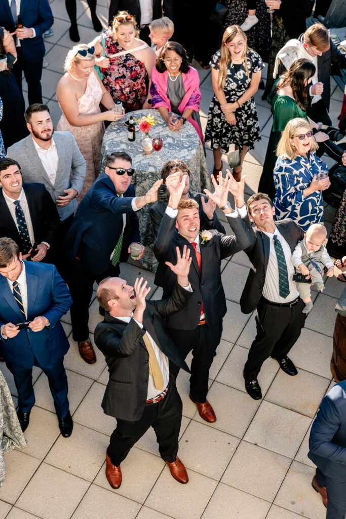 Guests jumping to catch a can coozie tossed by the groom in an action shot by the Catholic wedding photographer