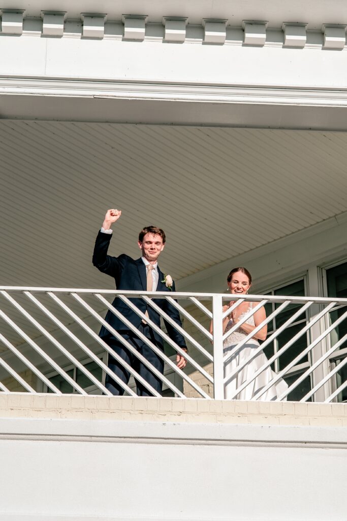 A bride and groom cheering from the balcony after their bouquet toss