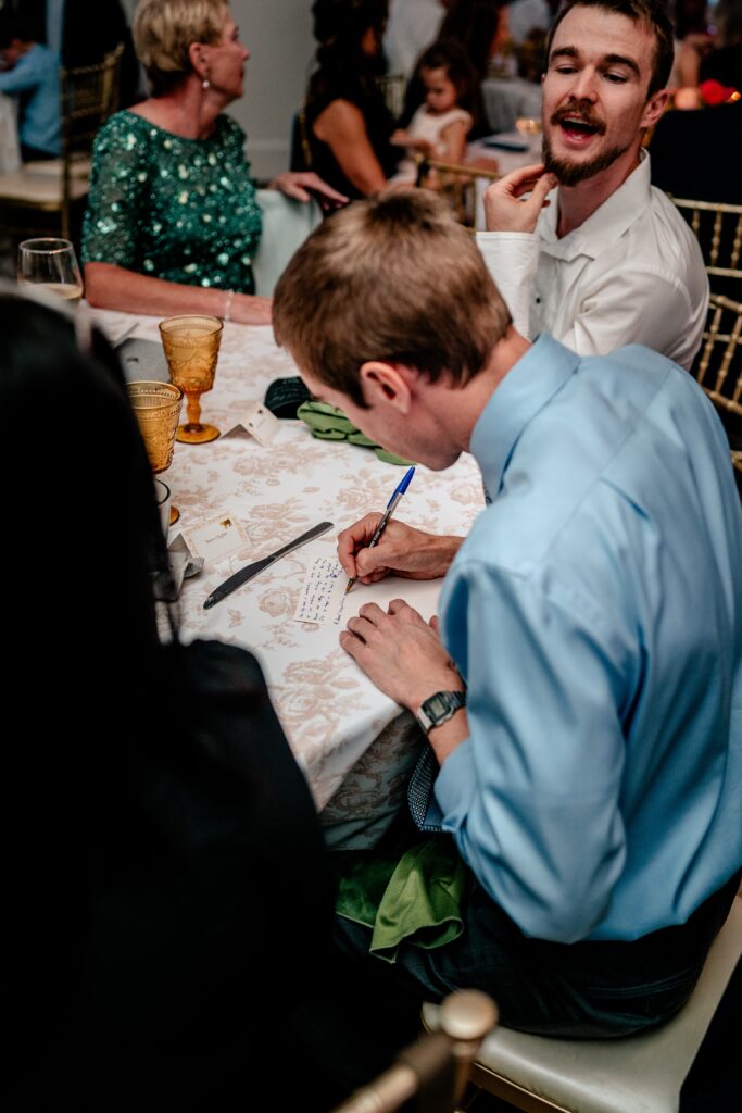 A wedding guest writing a note for the newlyweds in a candid by the Catholic wedding photographer