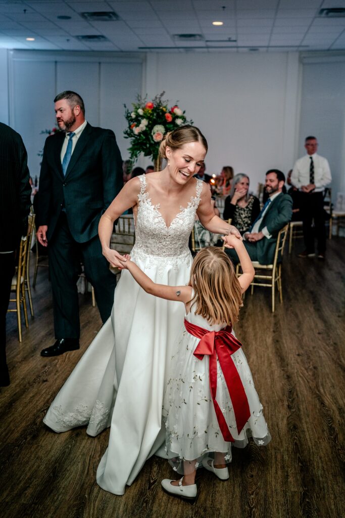 A bride dancing with a flower girl for the Catholic wedding photographer