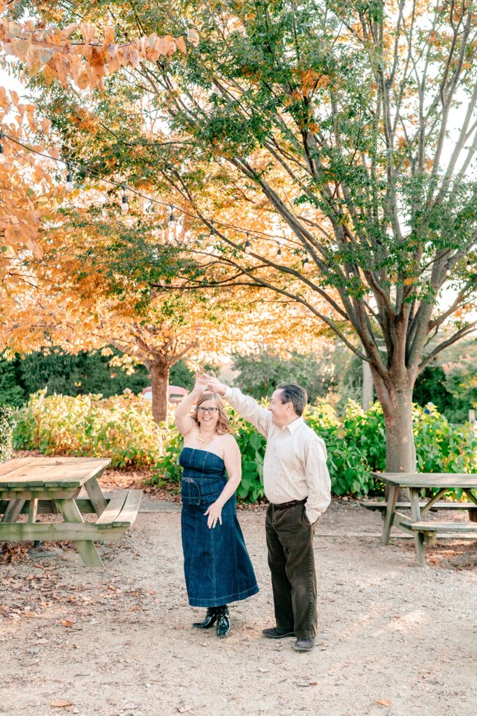 An engaged couple twirling under perfect fall foliage with their Catholic wedding photographer