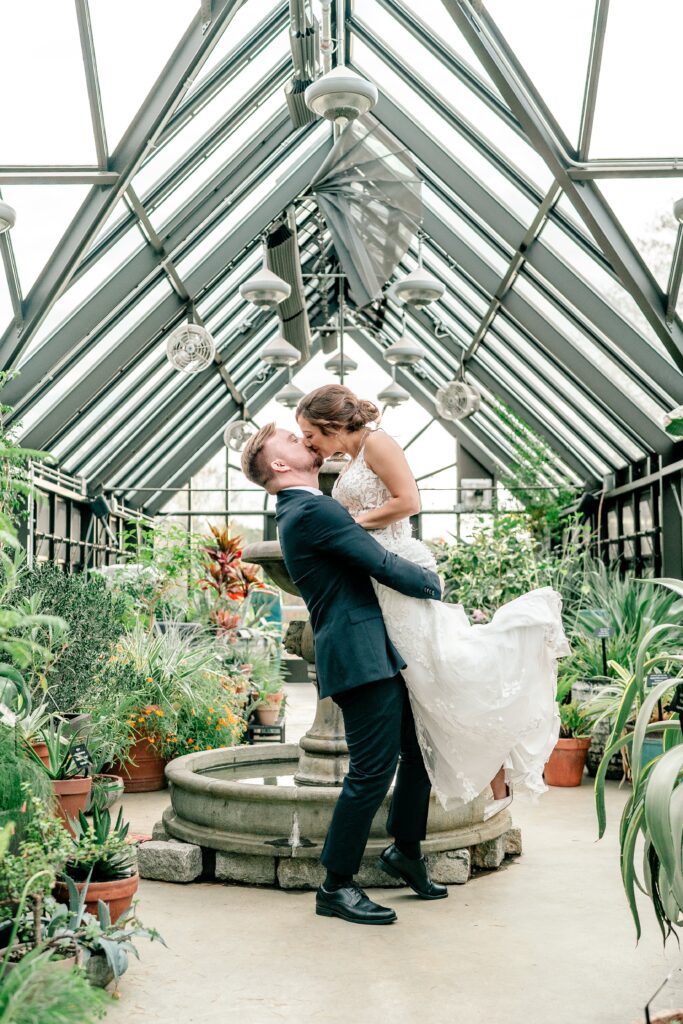 A couple sharing a romantic lift kiss inside a greenhouse wedding venue for their Virginia wedding photographer