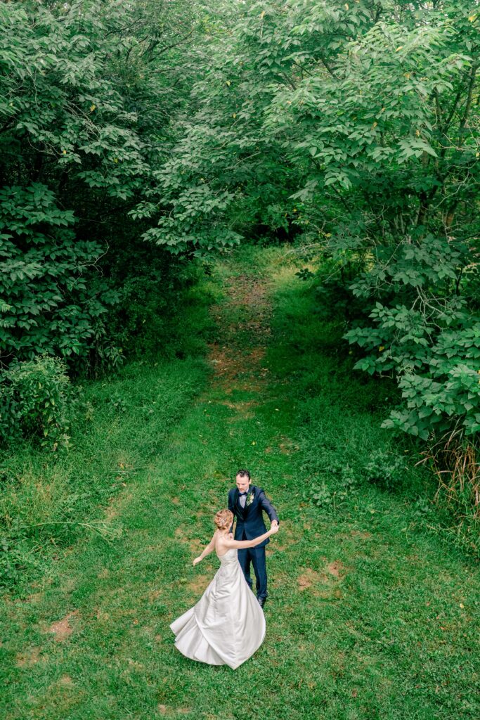 A bride and groom share a dance together in a field surrounded by trees