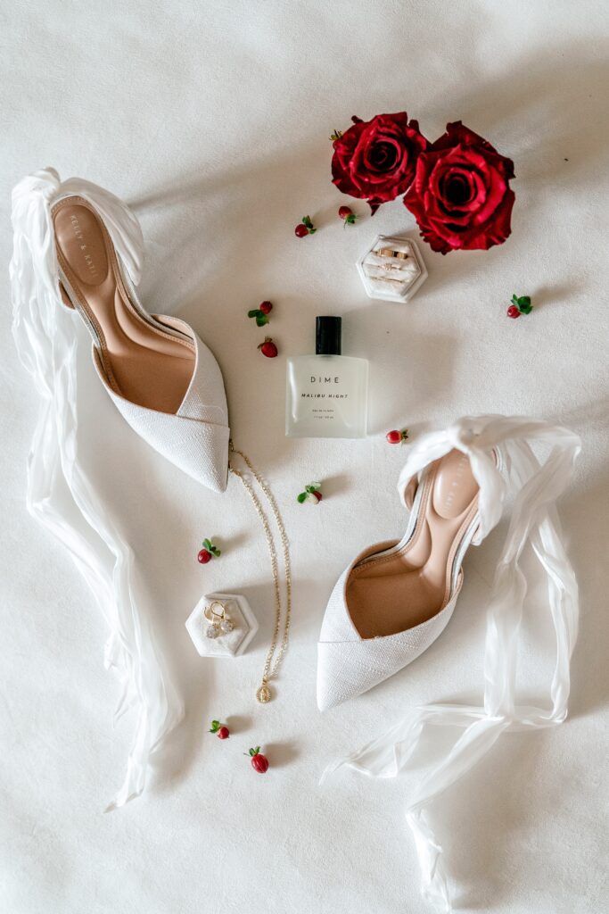 A flat lay of Christmas wedding details like romantic white bridal shoes and perfume before a St Francis de Sales wedding in Purcellville
