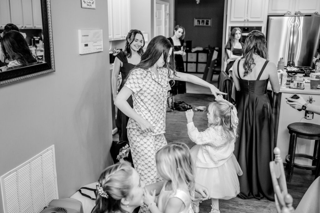 A bride in her getting ready pajamas dancing with a flower girl and surrounded by her bridesmaids in the kitchen