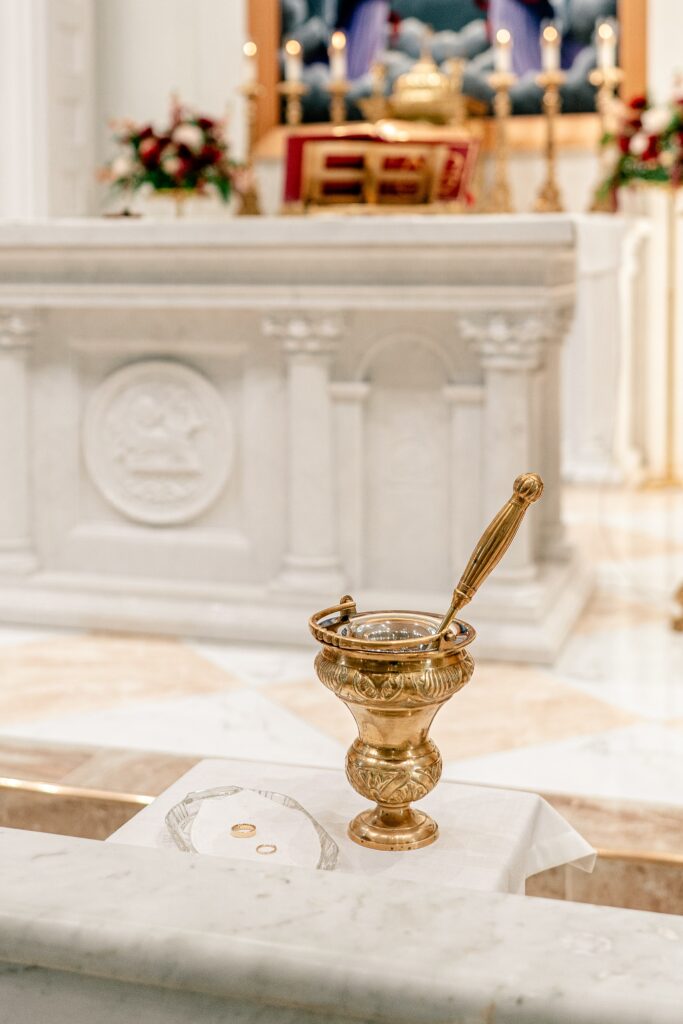 Wedding rings on a tray beside a container of holy water at the church before a wedding ceremony