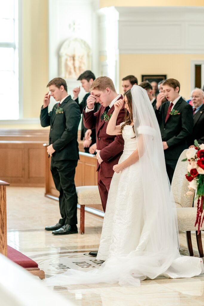 A bride and groom doing the sign of the cross on their foreheads before the Gospel reading of their St Francis de Sales wedding in Purcellville