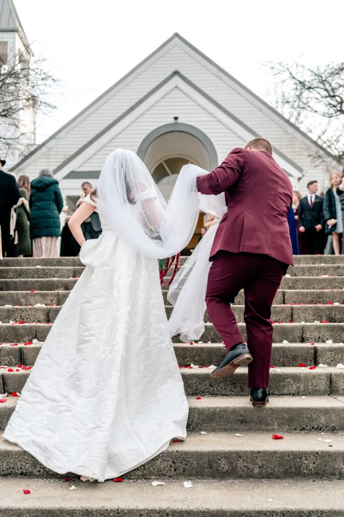 A bride and groom going up the stairs outside a church for their St Francis de Sales wedding in Purcellville