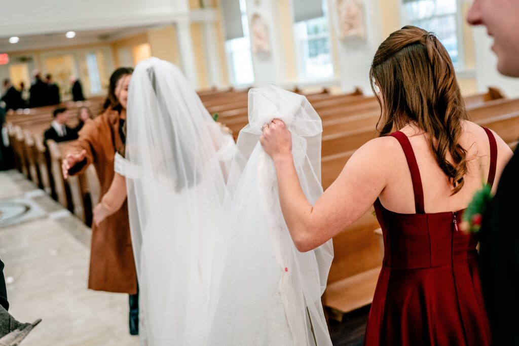 A bridesmaid holding the bride's veil as they walk through the church