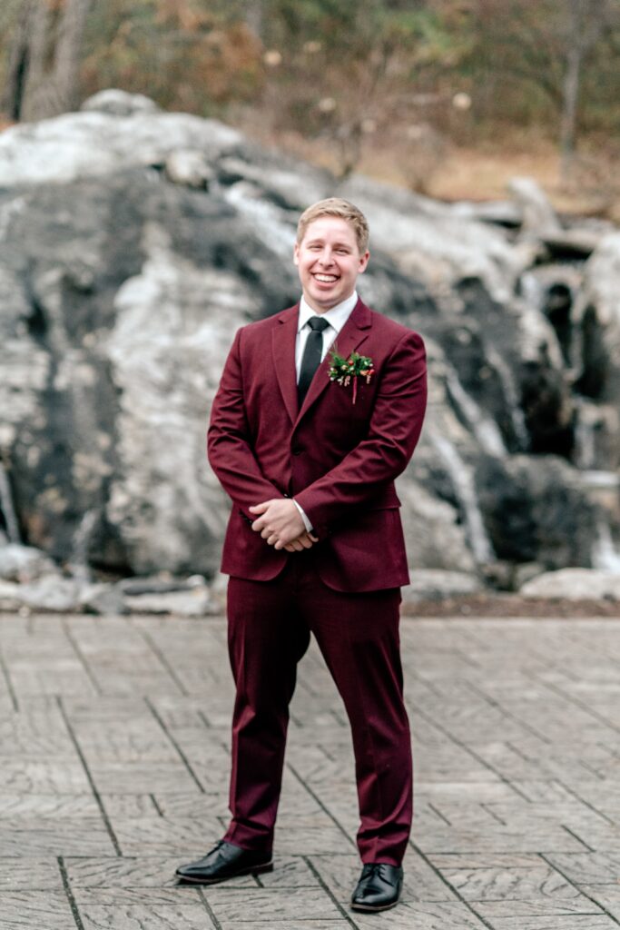 A groom smiling for a classic portrait in front of the waterfall during a Historic Rosemont wedding