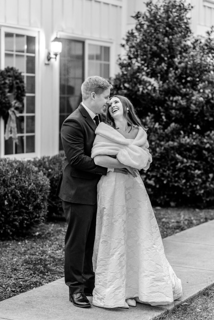 A bride and groom laughing together standing outside the barn during their Historic Rosemont wedding