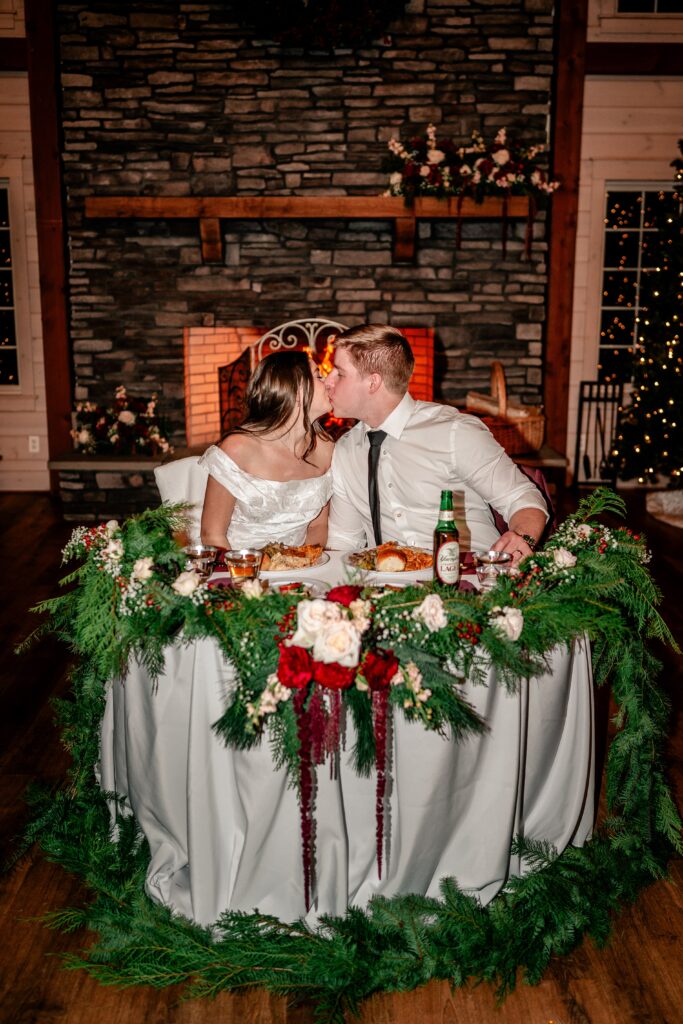 A bride and groom kiss at the sweetheart table in front of the fireplace during a Historic Rosemont wedding