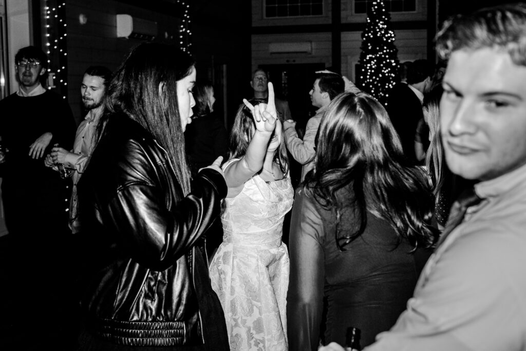A bride making the rock and roll hand gesture surrounded by guests on the dance floor