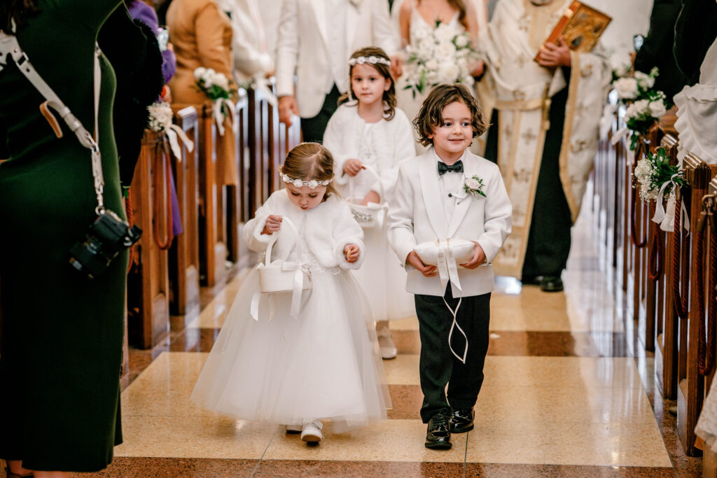 A pair of flower girls and ring bearer walking down the aisle