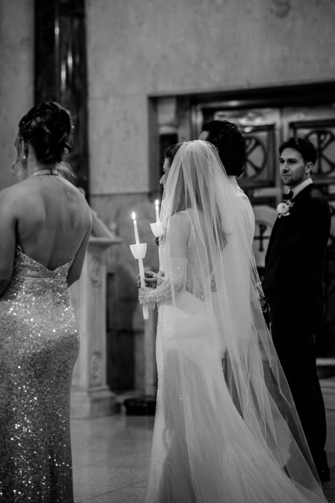 A bride and groom holding candles during their Greek Orthodox wedding ceremony