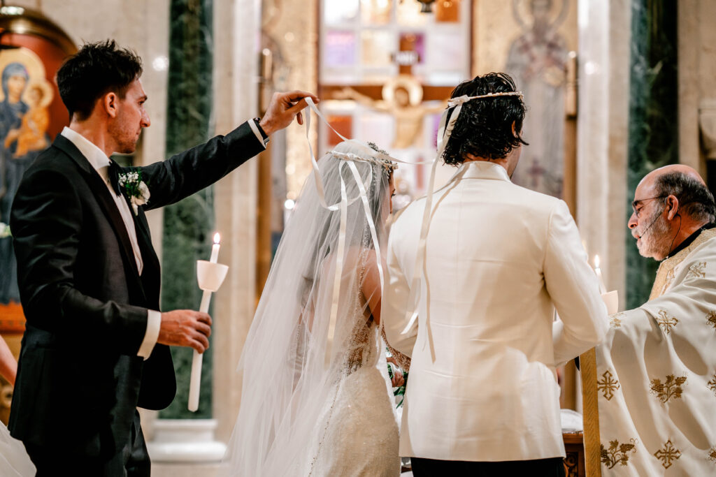 The best man holding up ribbons on the bride and groom's crowns during their Washington DC wedding