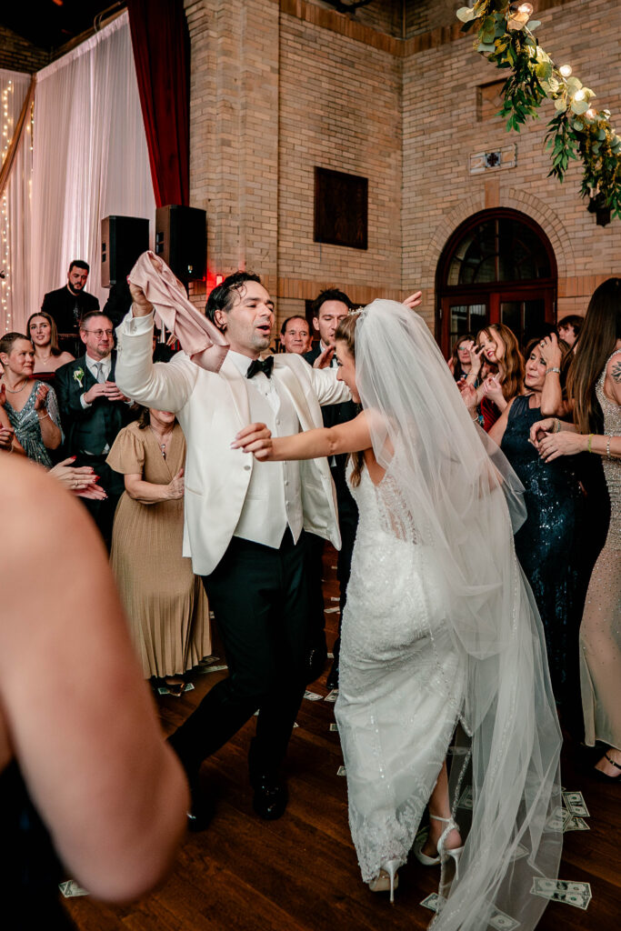 A groom dancing with his bride and waving a napkin during their Greek Orthodox wedding reception
