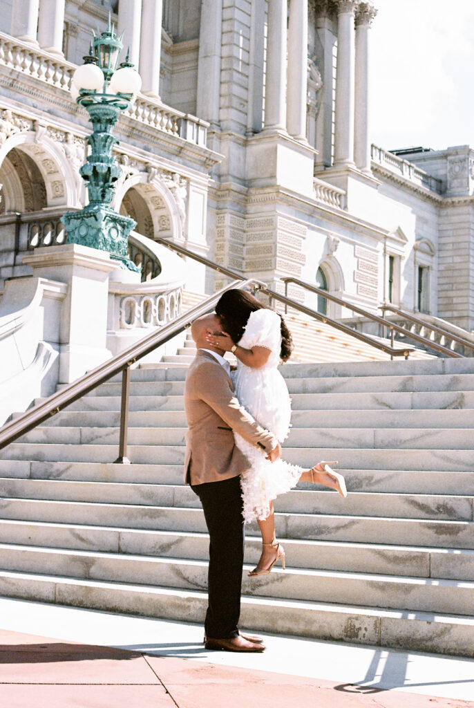 A couple sharing a dramatic kiss in front of the staircase during their film engagement photos