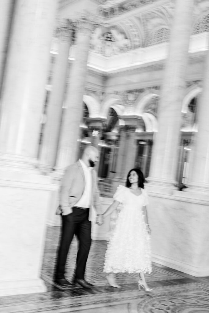 A blurry black and white shot of a couple walking hand in hand between marble columns