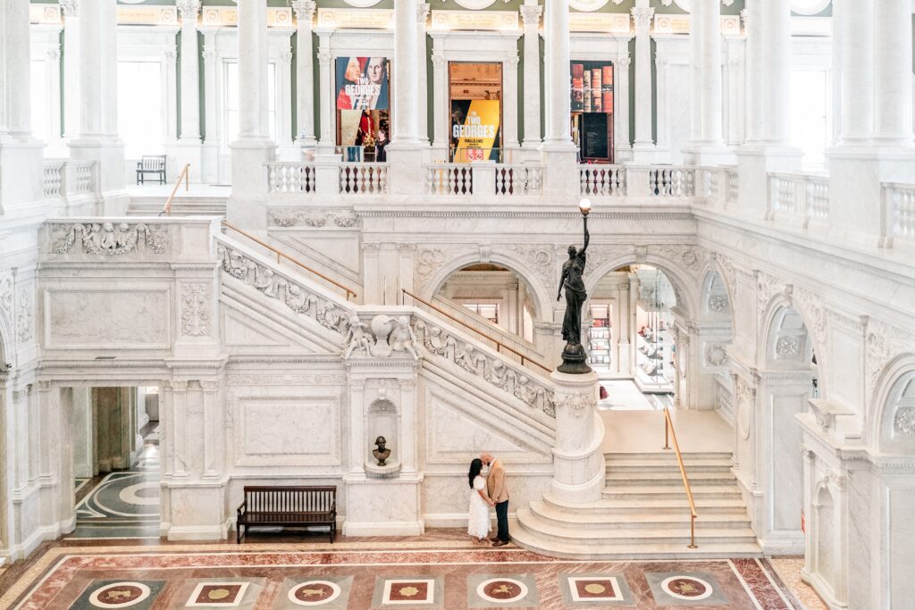A man and woman posed against the dramatic indoor staircase of the Library of Congress