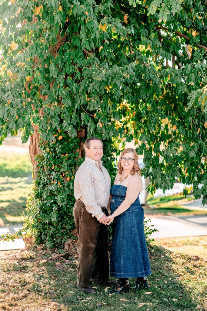 A couple posed while holding hands in front of a large tree