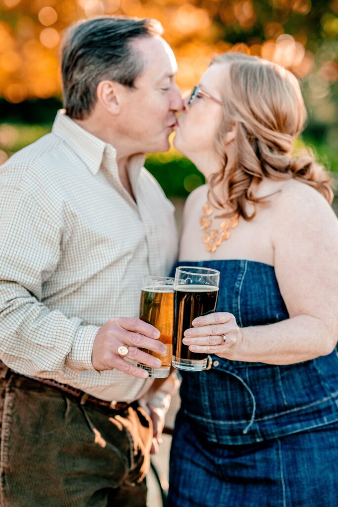 A couple shares a kiss as they toast their beers for their fall engagement photos near DC