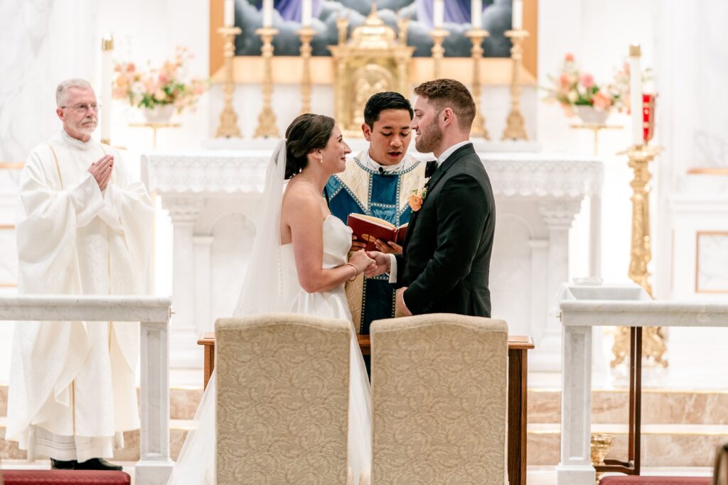 A bride and groom smiling at each other in front of the altar during their St. Francis de Sales wedding