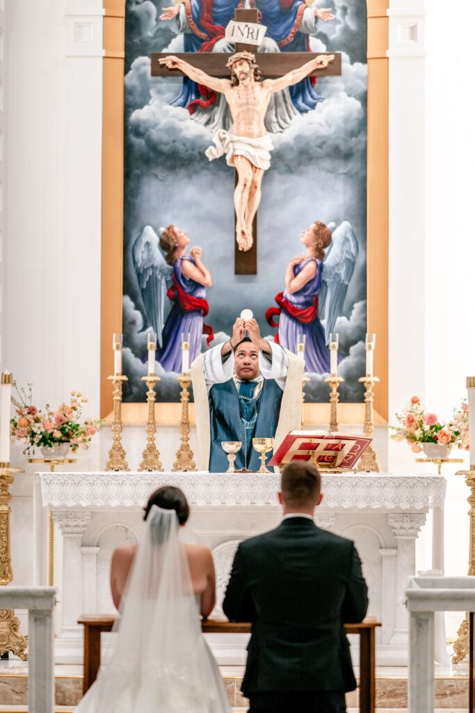 The priest holding up the Host at the Consecration by a Catholic wedding photographer