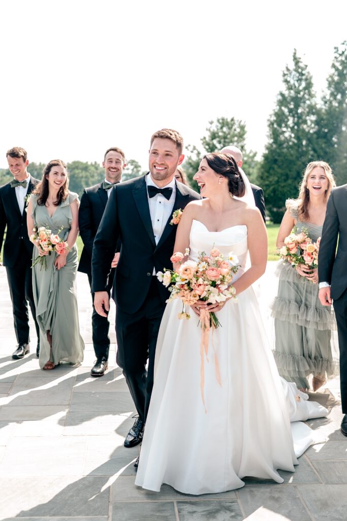 A bride and groom laughing as they walk with their wedding party after a St. Francis de Sales wedding