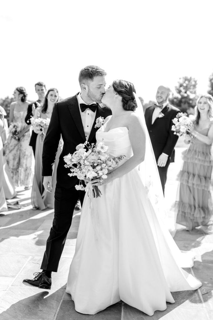 A bride and groom kiss as they walk with their wedding party