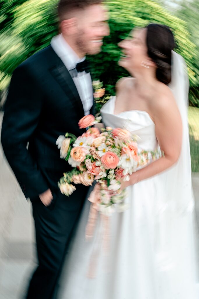 Motion blur centered on a peach bridal bouquet as a bride and groom smile at one another during their Shadow Creek wedding