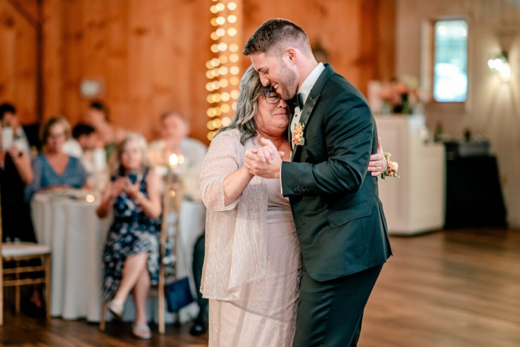 A groom dancing with his mom at his barn reception after a St. Francis de Sales wedding
