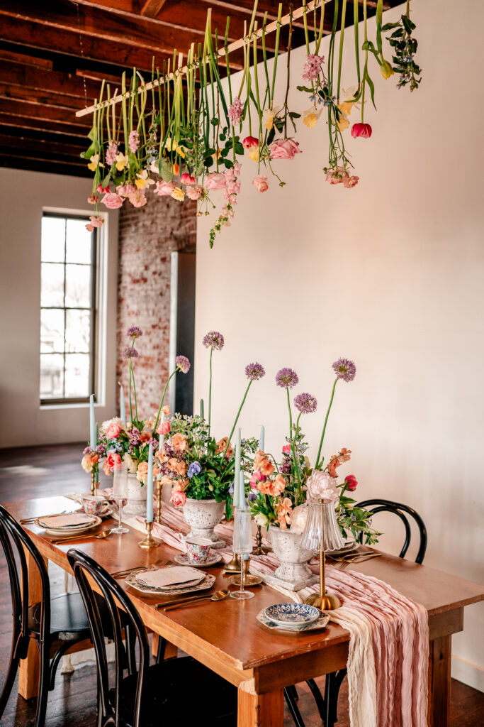 A reception table with playful floral centerpieces and flowers hanging overhead for a tea party wedding