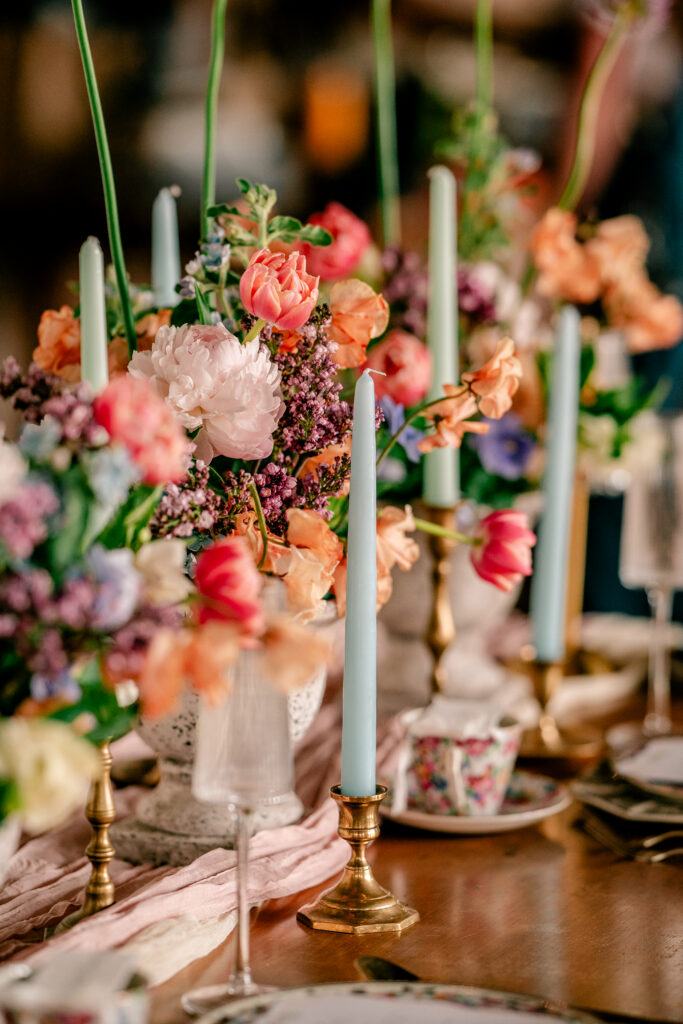 A blue taper candle in front of a colorful flower arrangement