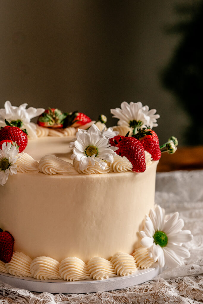 An ivory buttercream cake with white daisies and strawberries